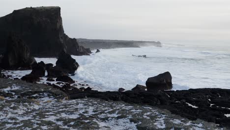Grand-cliff-coastal-landscape-of-Iceland-with-rugged-volcanic-land,-waves-crashing-on-shore