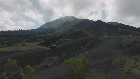 Jeep-drives-up-sandy-slope-of-Mount-Batur-with-tourist,-cinematic-reveal-shot
