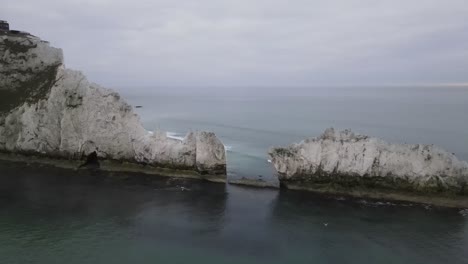 4K-30FPS-Aerial-drone-flight-alongside-the-white-cliffs-of-The-Needles-in-the-Isle-of-Wight-showing-a-red-and-white-lighthouse-and-waves-crashing-against-the-rocks