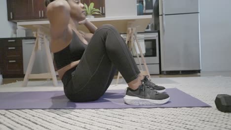 A-sliding-shot-of-a-black-female-doing-sit-ups-in-her-kitchen