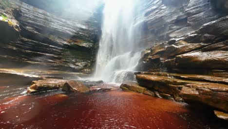 Tilting-up-slow-motion-action-camera-shot-from-the-base-of-the-Mosquito-Waterfall-surrounded-by-plants-and-cliffs-and-a-river-below-in-the-Chapada-Diamantina-National-Park-in-Northeastern-Brazil
