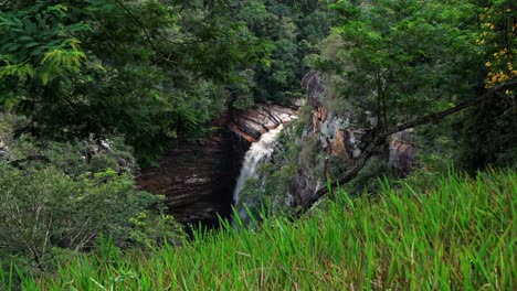 Beautiful-tilting-down-4K-shot-of-the-Mosquito-Falls-from-a-hike-lookout-surrounded-by-jungle-foliage-and-cliffs-in-the-Chapada-Diamantina-National-Park-in-Northeastern-Brazil-on-a-summer-day