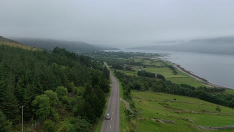 A-drone-shot-following-a-car-down-to-Ullapool,-Scotland,-on-a-misty-day