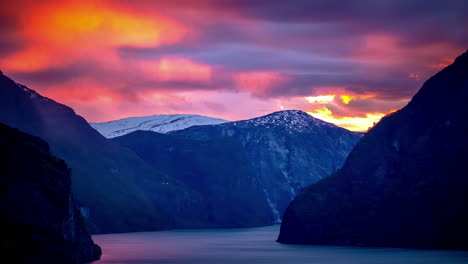 Brilliant-sunset-pink-and-purple-clouds-cross-the-sky-above-steep-mountainsides-plummeting-into-a-misty-fjord-in-Scandinavia---time-lapse