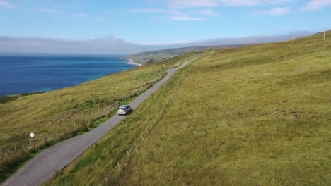 Stunning-drone-shot-following-a-car-along-a-hilltop-road-beside-the-sea-in-north-east-Scotland-near-Melvaig