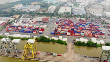 Stacked-containers-at-river-port,-drone-tilt-down-reveals-port-cranes,-Saigon