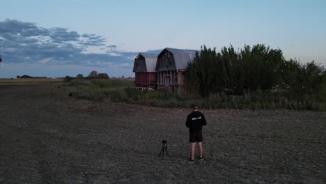 Photographer-taking-picture-of-abandoned-farm-buildings-with-a-camera-on-a-small-tripod