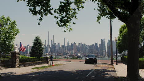New-Jersey-Street-With-Waving-Flag,-Pedestrian-And-Black-SUV-Passing,-Overlooking-Manhattan,-New-York-City,-U