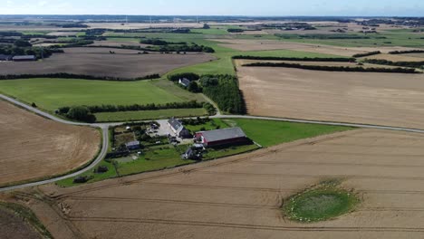 Drone-circles-over-a-farm-in-a-beautiful-landscape-in-northwestern-Denmark,-super-great-weather