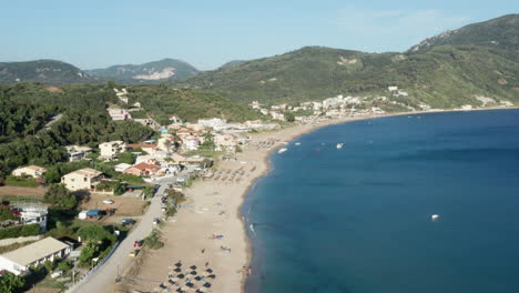 Aerial-shot-of-a-Mediterranean-beach,-right-below-the-green-forest-covered-mountains