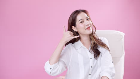 Young-Asian-woman-making-phone-call-motion-with-hands-in-the-studio-with-pink-background