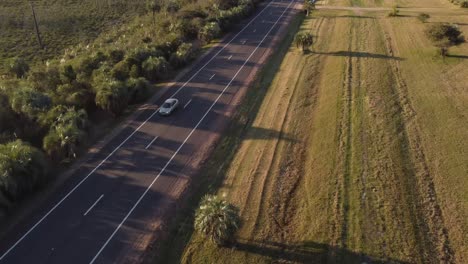 Drone-shot-of-car-driving-on-rural-road-at-sunset-in-Uruguay---Travelling-in-scenic-area-of-South-America