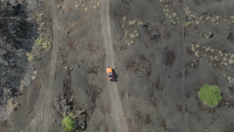 Orange-jeep-driving-on-basalt-sand-path,-4x4-car-off-road-on-old-lava-field,-top-down