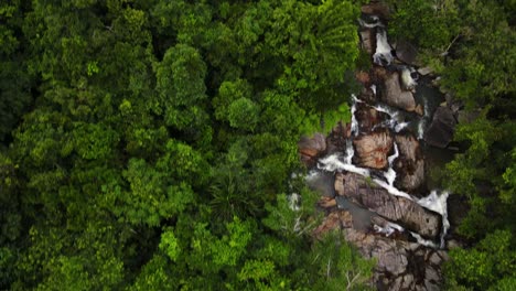 Drone-aerial-camera-flying-along-a-mountain-waterfall-and-dense-greenery-in-Thailand's-evergreen-Than-Sadet-waterfall-region