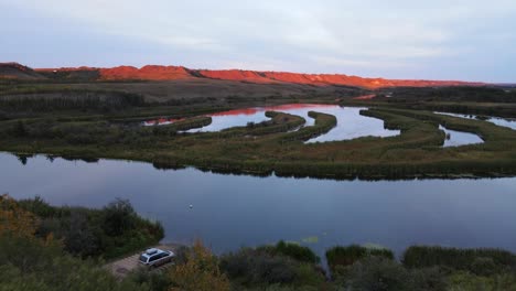 Letztes-Orangefarbenes-Sonnenlicht,-Das-Die-Gipfel-Einer-Bergkette-Im-Südlichen-Alberta-Beleuchtet,-Mit-Wunderschönen-Reflexionen-Auf-Dem-Ruhigen-Fluss-Davor