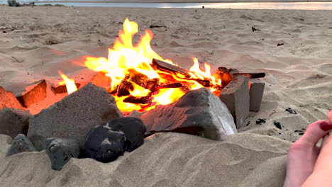 Slow-motion-parallax-of-beach-campfire,-revealing-feet-of-woman-enjoying-evening
