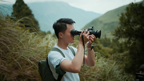 A-young-Asian-male-photographer-in-a-white-T-shirt-and-a-backpack-is-taking-photographs-of-nature-in-the-mountains-in-northern-Taiwan