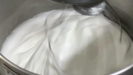 Soft-and-fluffy-meringue-buttercream-pastry-making-in-progress,-commercial-kitchen-setting-close-up-shot-of-an-electric-mixer-mixing-egg-white-and-sugar-until-it-is-glossy-peak-and-stiff-peak