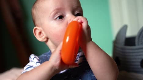 Close-up-of-6-month-old-baby-boy-chewing,-teething,-and-gumming-on-toy,-playing-in-nursery
