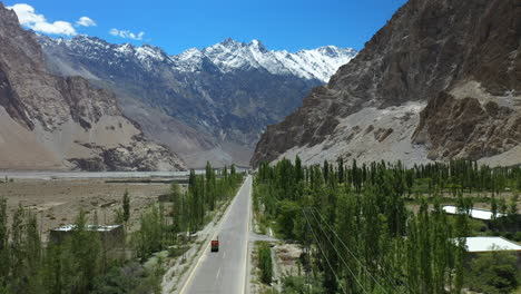 Cinematic-aerial-shot-of-Tupopdan-Peak,-Passu-Cones-in-Hunza-Pakistan,-tracking-a-Tuk-Tuk-driving-on-Karakoram-Highway,-drone-shot