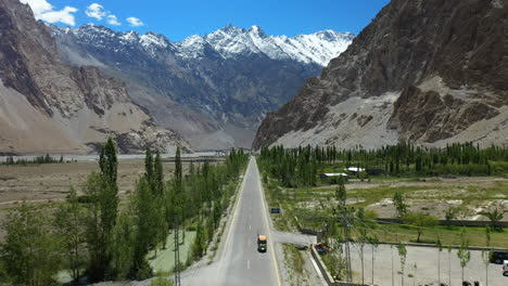 Cinematic-drone-shot-of-Passu-Cones-in-Hunza-Pakistan,-Tuk-Tuk-driving-on-Karakoram-Highway-with-Tupopdan-Peak-in-the-background