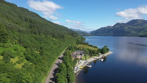 Slow-drone-shot-of-the-A82-on-Loch-Lomond,-just-north-of-Luss-on-a-beautiful,-summer-day