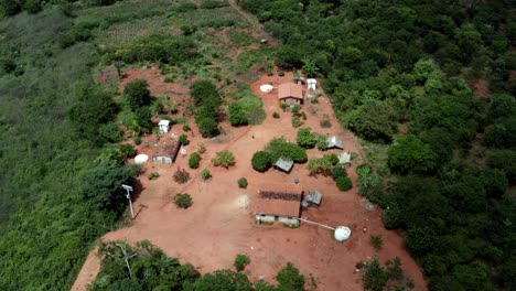 Rotating-aerial-drone-shot-of-a-Brazilian-farm-in-the-Chapada-Diamantina-National-park-in-Northern-Brazil-with-various-houses-surrounded-by-green-trees,-red-dirt,-and-a-man-walking-around