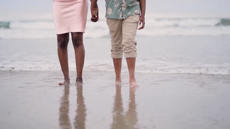 Afroamerikanisches-Paar,-Das-Händchen-Hält-Und-Am-Strand-Spazieren-Geht,-Vorderansicht-Von-Zwei-Liebenden-Mit-Dem-Meer-Dahinter