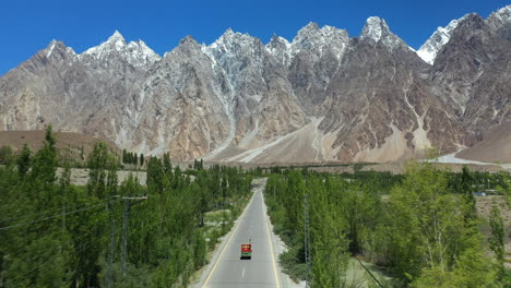 Cinematic-drone-shot-of-Passu-Cones-in-Hunza-Pakistan,-moving-towards-the-Tupopdan-Peak-tracking-a-Tuk-Tuk-driving-on-Karakoram-Highway,-aerial-shot