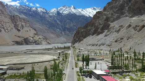Cinematic-drone-shot-of-Passu-Cones-in-Hunza-Pakistan,-moving-away-from-Tupopdan-Peak-tracking-a-Tuk-Tuk-driving-on-Karakoram-Highway,-aerial-shot