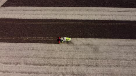 Top-down-drone-footage-of-a-dark-feed-bean-field-being-harvested-by-a-combine-harvester