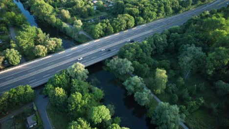 Aerial-top-down,-cars-driving-on-rural-highway-bridge-over-river-stream,-surrounded-by-lush-green-trees-in-Brunswick,-Germany