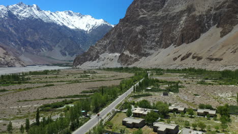 Toma-Cinematográfica-De-Drones-De-Conos-Passu-En-Hunza-Pakistán,-Moviéndose-Hacia-El-Pico-Tupopdan-Con-Un-Tuk-Tuk-Conduciendo-En-La-Autopista-Karakoram,-Toma-Aérea-Amplia-1