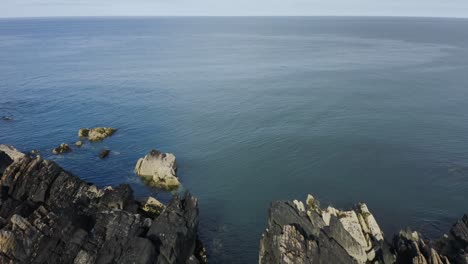 Drone-is-flying-towards-the-sea-along-the-rocky-shore-of-Clogherhead,-Ireland