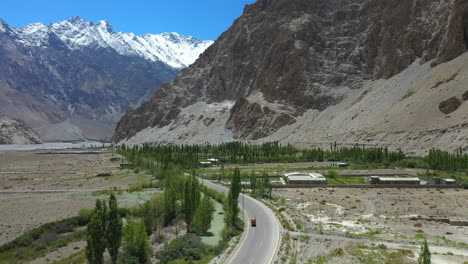 Cinematic-drone-shot-of-Passu-Cones-in-Hunza-Pakistan,-moving-towards-the-Tupopdan-Peak-with-a-Tuk-Tuk-driving-on-Karakoram-Highway,-wide-shot