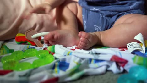 Close-up-of-baby-feet-while-infant-is-playing-with-rattle,-teething-ring-on-blanket