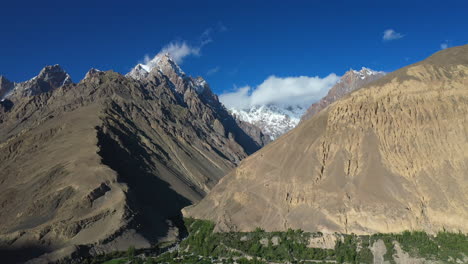 Cinematic-drone-shot-of-Tupopdan-Peak,-Passu-Cones-in-Hunza-Pakistan,-snow-covered-mountain-peaks-with-steep-cliffs-and-clouds-forming-on-top,-high-rising-wide-aerial-shot
