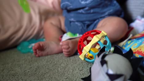 Close-up-of-6-month-old-infant-playing-with-ball-rattle,-teething-ring-on-blanket