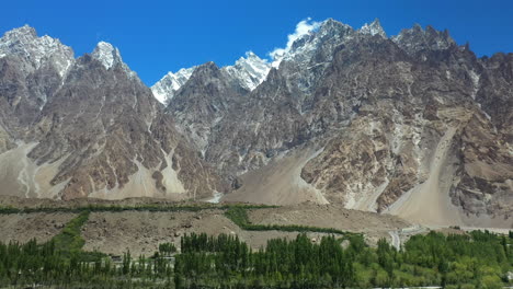 Cinematic-drone-shot-of-Tupopdan-Peak-from-the-valley,-Passu-Cones-in-Hunza-Pakistan,-snow-covered-mountain-peaks-with-steep-cliffs,-wide-panning-aerial-shot