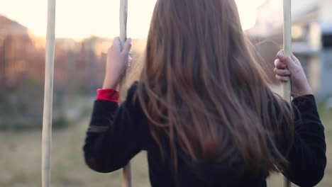 Little-girl-playing-alone-on-the-swings-of-a-swing-set-hair-blowing-in-the-breeze-late-afternoon-sunset-b-roll