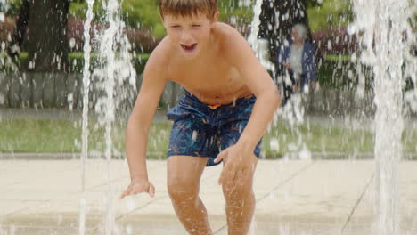 Young-boy-is-sitting-and-running-in-public-water-fountain,-carefree-childhood,-slow-motion