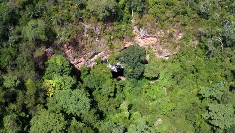 Rising-aerial-drone-shot-of-the-cave-entrance-to-the-Enchanted-Well-or-Poço-Encantado-surrounded-by-tropical-trees,-plants,-and-cliffs-in-the-Chapada-Diamantina-National-Park-in-Northern-Brazil