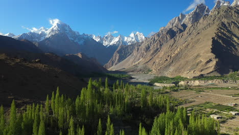 Drone-shot-of-Tupopdan-Peak,-Passu-Cones-in-Hunza-Pakistan,-snow-covered-mountain-peaks-with-steep-cliffs,-starting-in-the-valley-on-trees-then-tilting-up-to-reveal-mountains