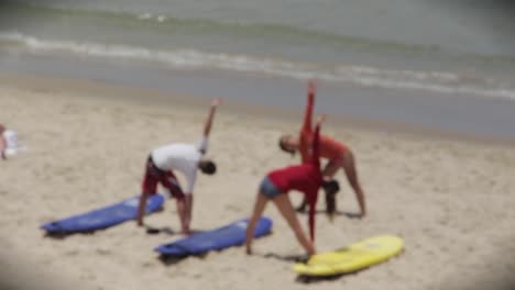 Tiro-Borroso-De-Surfistas-Estirándose-En-La-Playa-Con-Movimientos-De-Yoga,-Haciendo-Ejercicio-Y-Practicando