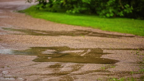 Close-up-shot-over-rain-falling-over-gravel-pathway-creating-puddles-in-rural-landscape-on-a-rainy-day