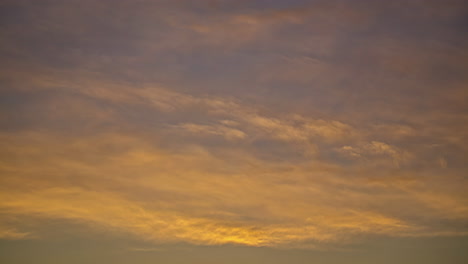 Low-angle-shot-of-thick-clouds-passing-by-in-timelapse-with-yellow-rays-along-the-setting-sun