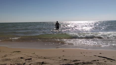 Caucasian-middle-aged-male-walking-in-swimsuit-into-Lake-Michigan-water-on-the-beach