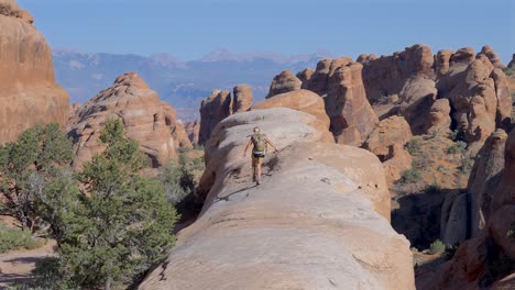 Blonde-female-hiking-walking-up-a-unique-rock-formation-in-Arches-National-Park,-Utah