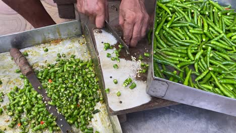 A-poor-man-is-shown-up-close-using-an-iron-knife-to-chop-a-lot-of-green-chilies-or-Mirchi-at-a-roadside-Dhaba