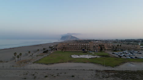 Sonnenuntergangsdrohnenaufnahme,-Die-Sich-über-Dem-Strandresort-Erhebt-Und-Von-Spanien-Aus-Nach-Süden-In-Richtung-Afrika-Blickt,-Mit-Dem-Felsen-Von-Gibraltar-Im-Blick